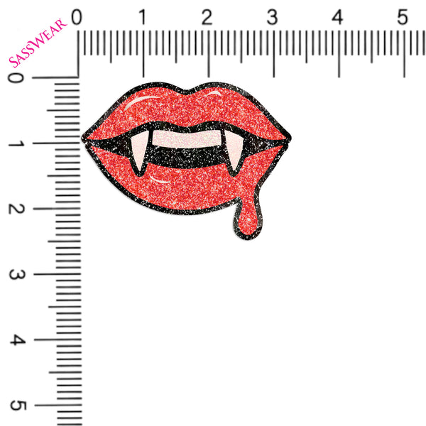 Lip patch with vampire teeth design next to a ruler for scale on a white background